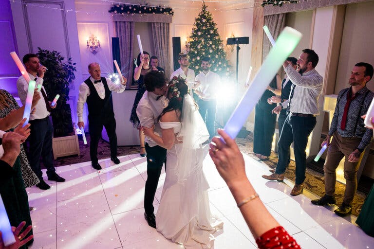 Maxine & Alastair's wedding reception. Guests dance on the dance floor with glow sticks surrounding the bride and groom.