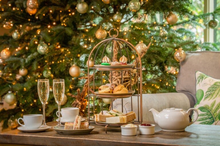Festive afternoon tea is served with a Christmas tree in the background at Careys Manor Hotel