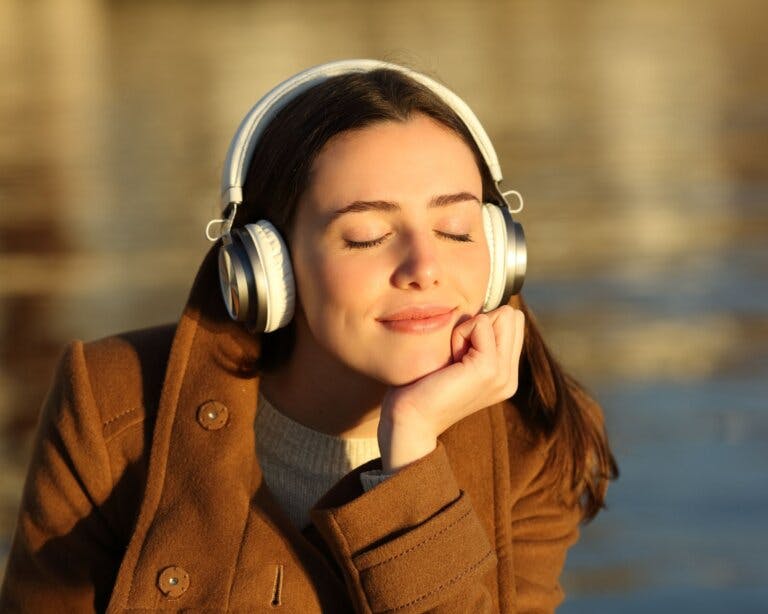A women with long brown hair is listening to calming music on headphone. She looks relaxed.