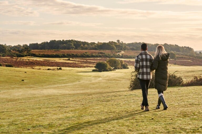 a man and a women walking arm in arm through open heathland in Autumn in the New Forest