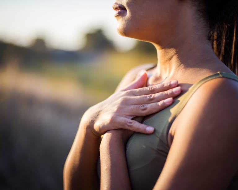 Lady with her hand on her chest taking deep breaths. the image is from her chin to her chest