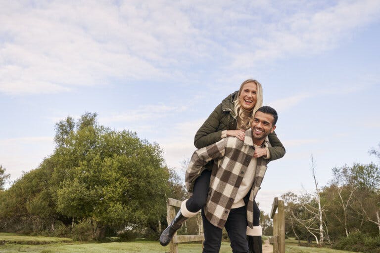 A man giving a piggy back to a lady who are both smiling in the New Forest