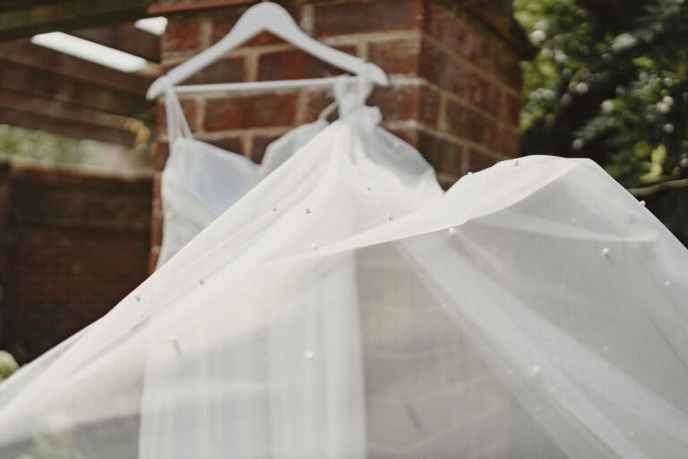 Wedding dress hanging in the garden, close up of the top of the dress with the veil blowing in the wind in front of the camera.