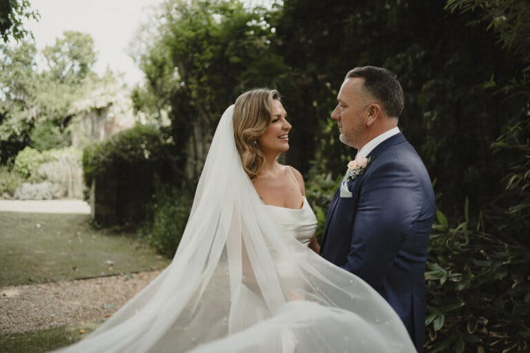 The bride and groom are photographed in the grounds while the veil blows in the wind