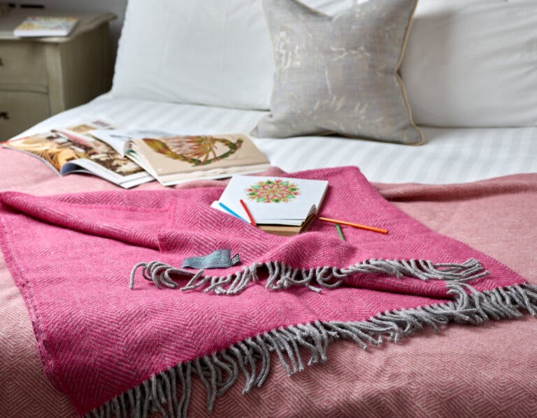 Mindful adult colouring books onto of bed with a pink wool blanket draped over the end