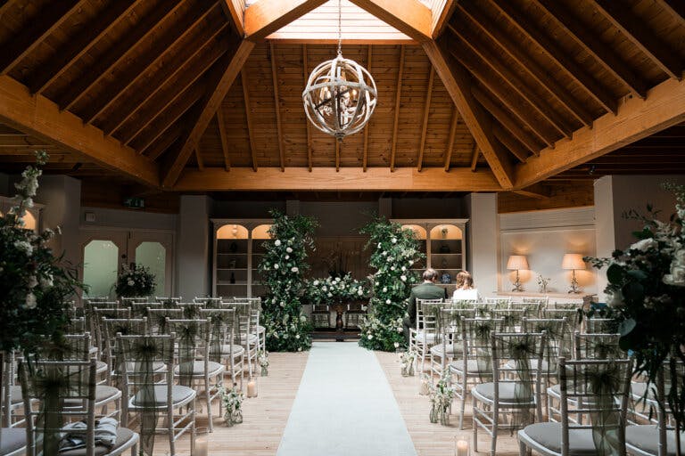 View of the lounge looking down the aisle towards the registras table. In front of the table is a large green and white floral decoration which appears as an 'H' as it runs along the table and has two high sides