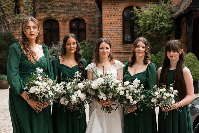 The bride and bridesmaids stand outside and pose in a line with their bouquets