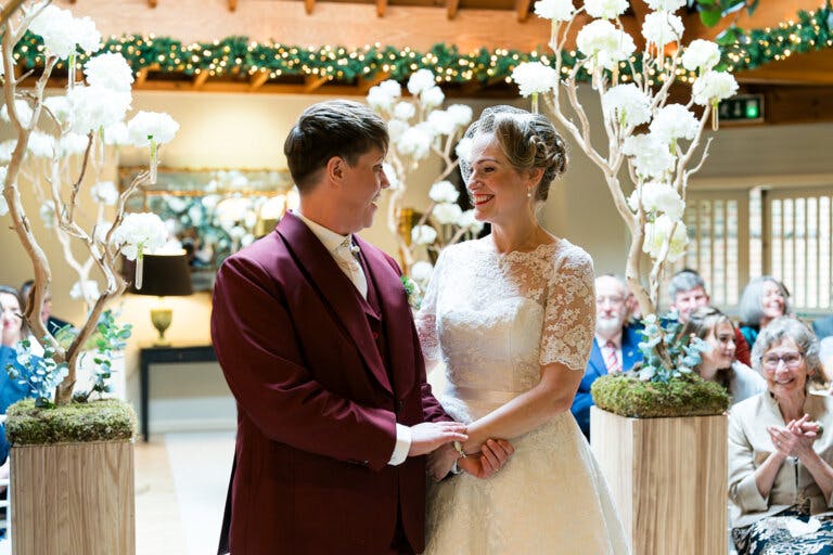Close shot of the couple facing each other, smiling and holding hands during the wedding ceremony