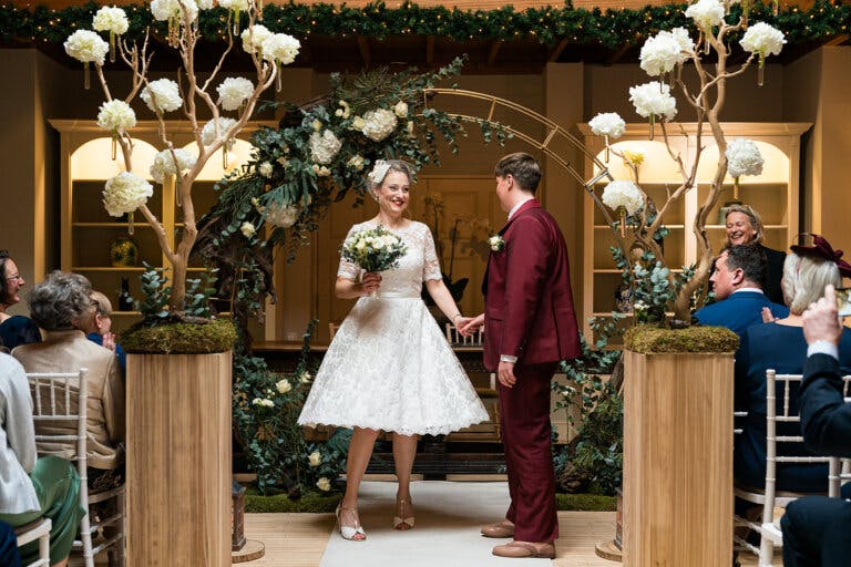 The brides stand in front of the moon arch smiling at each other in front of the registrars table