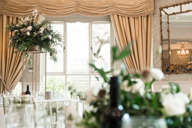 A view through the tables, showing white flowers and a curtained window