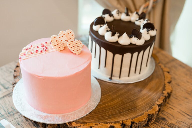The image shows two wedding cakes, one pink and one chocolate