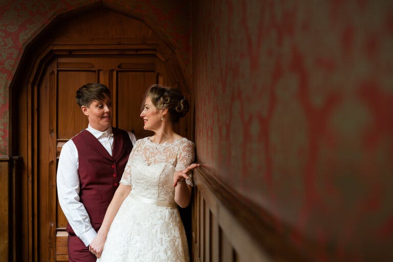 The Brides stand at the top of the staircase whilst leaning on the banister, looking at each other.