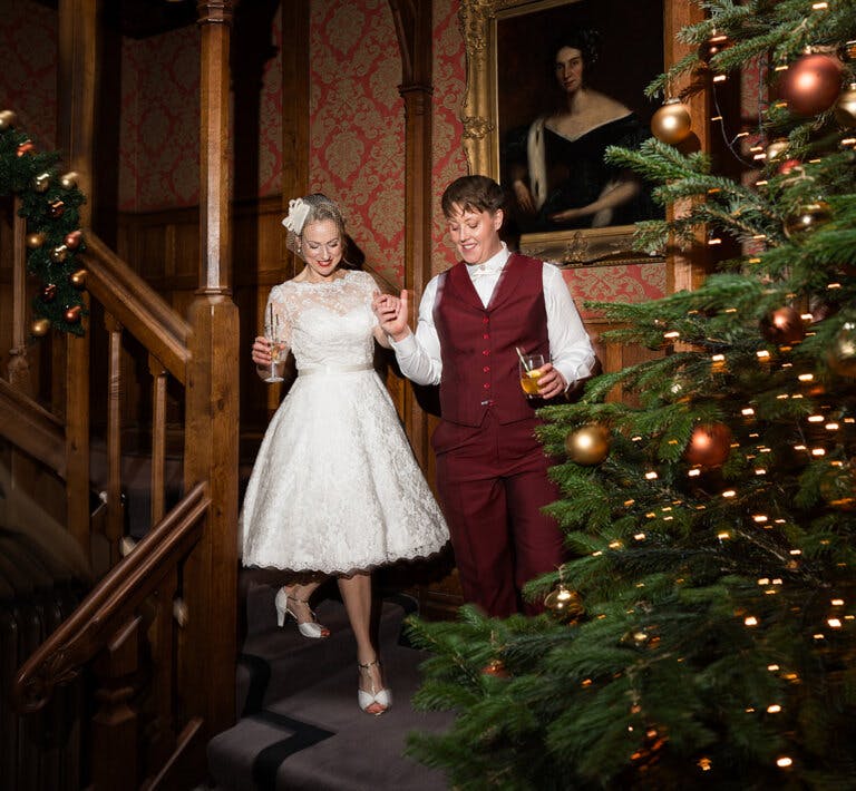 The brides walk down the staircase hand in hand with the Christmas tree on the right of the image.