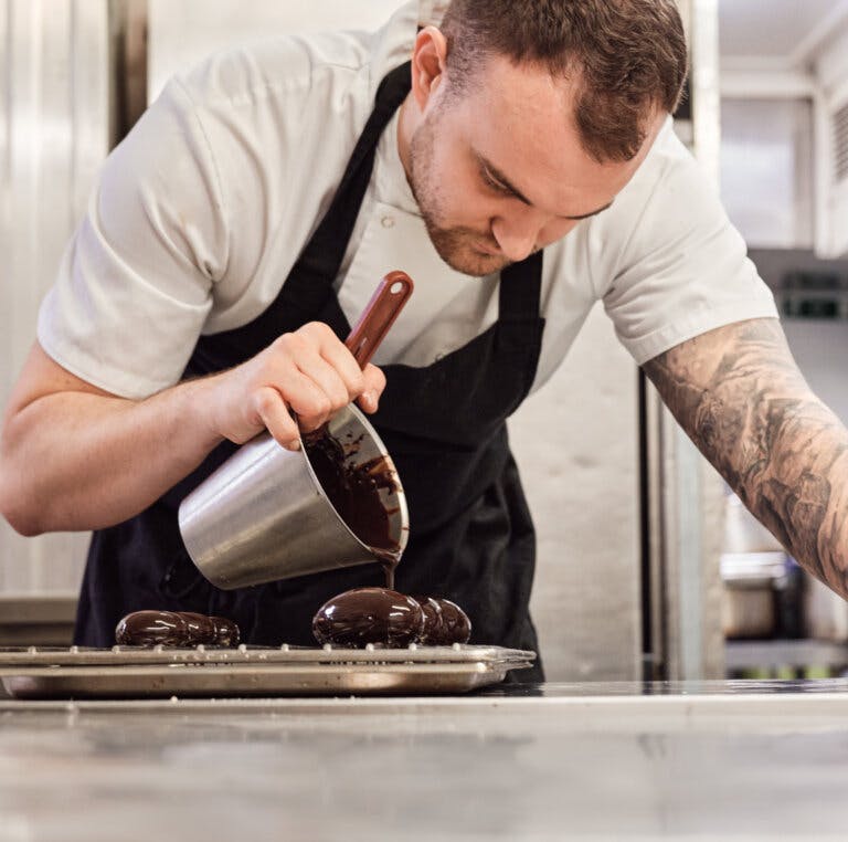 Pastry chef working in the kitchen pouring chocolate over small eggs