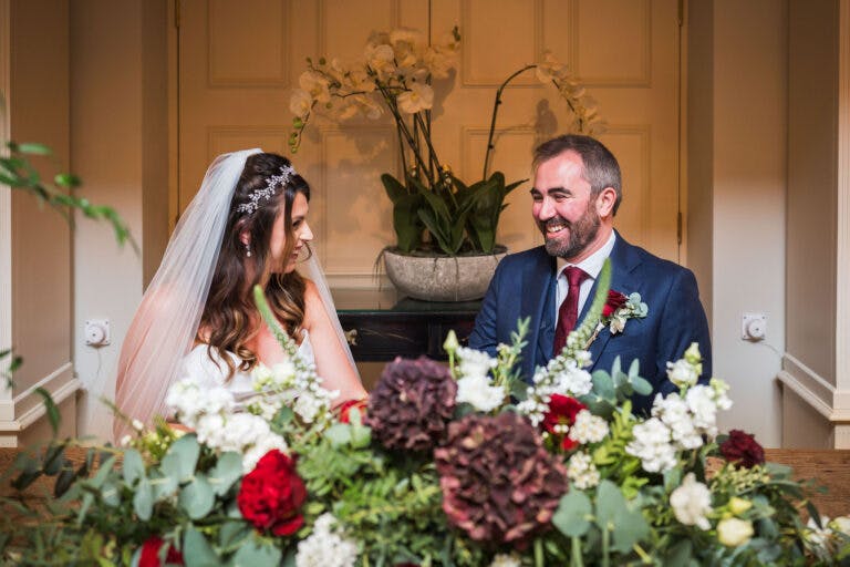 Bride & Groom sit behind the registrars table, smiling at each other