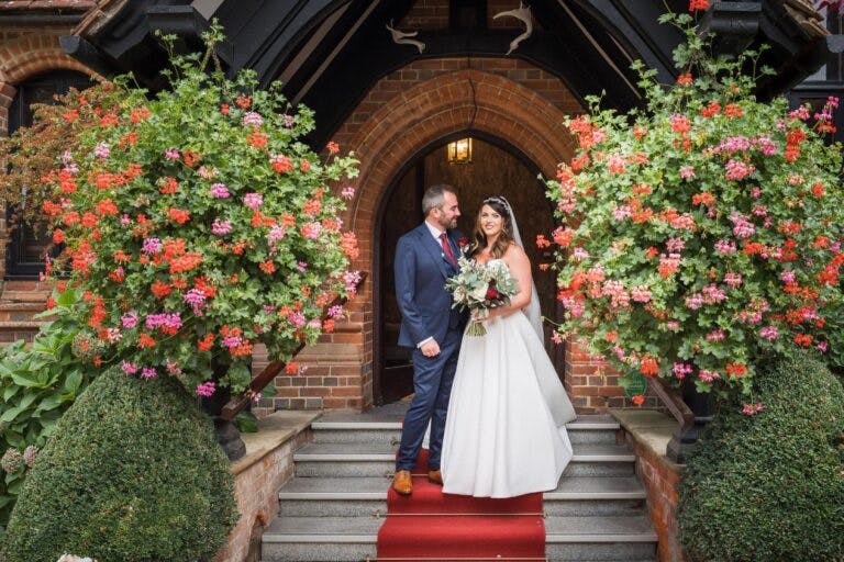 Bride and groom stood at hotel entrance flanked by large beautiful hanging baskets