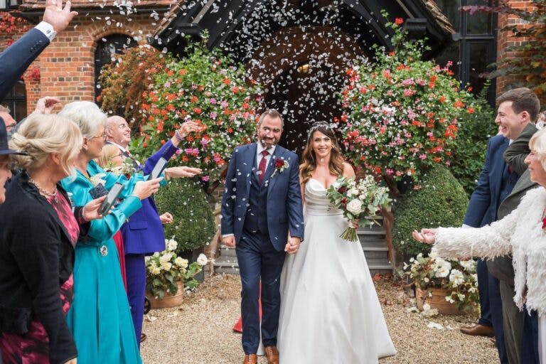 Chloe & Sam walk through an aisle of their guests throwing confetti at the entrance to the hotel