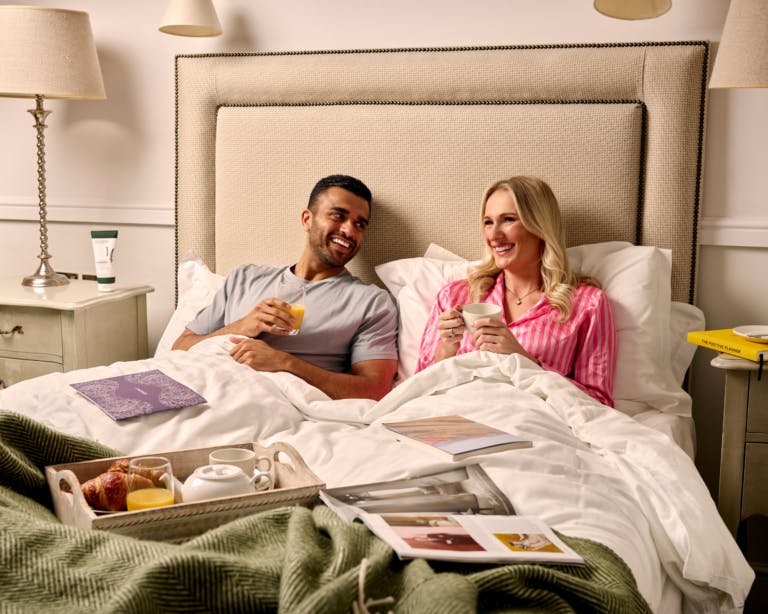 Couple in bed at hotel enjoying breakfast