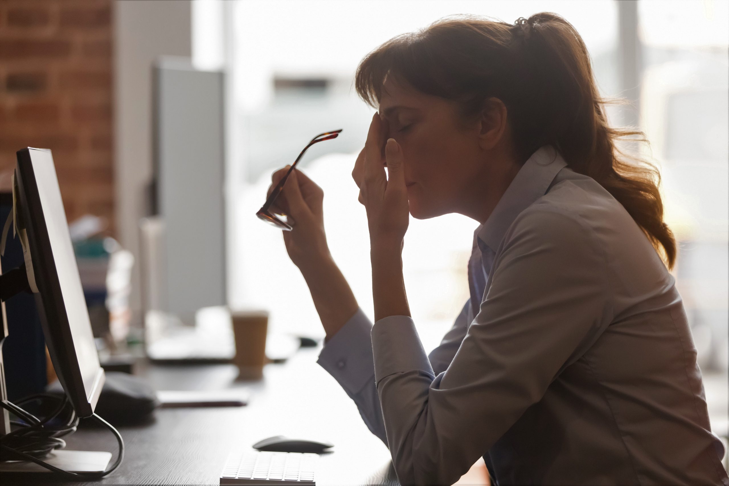 Young adult woman wearing a business suit taking off her glasses in despair as she displays staff negativity after returning back to work