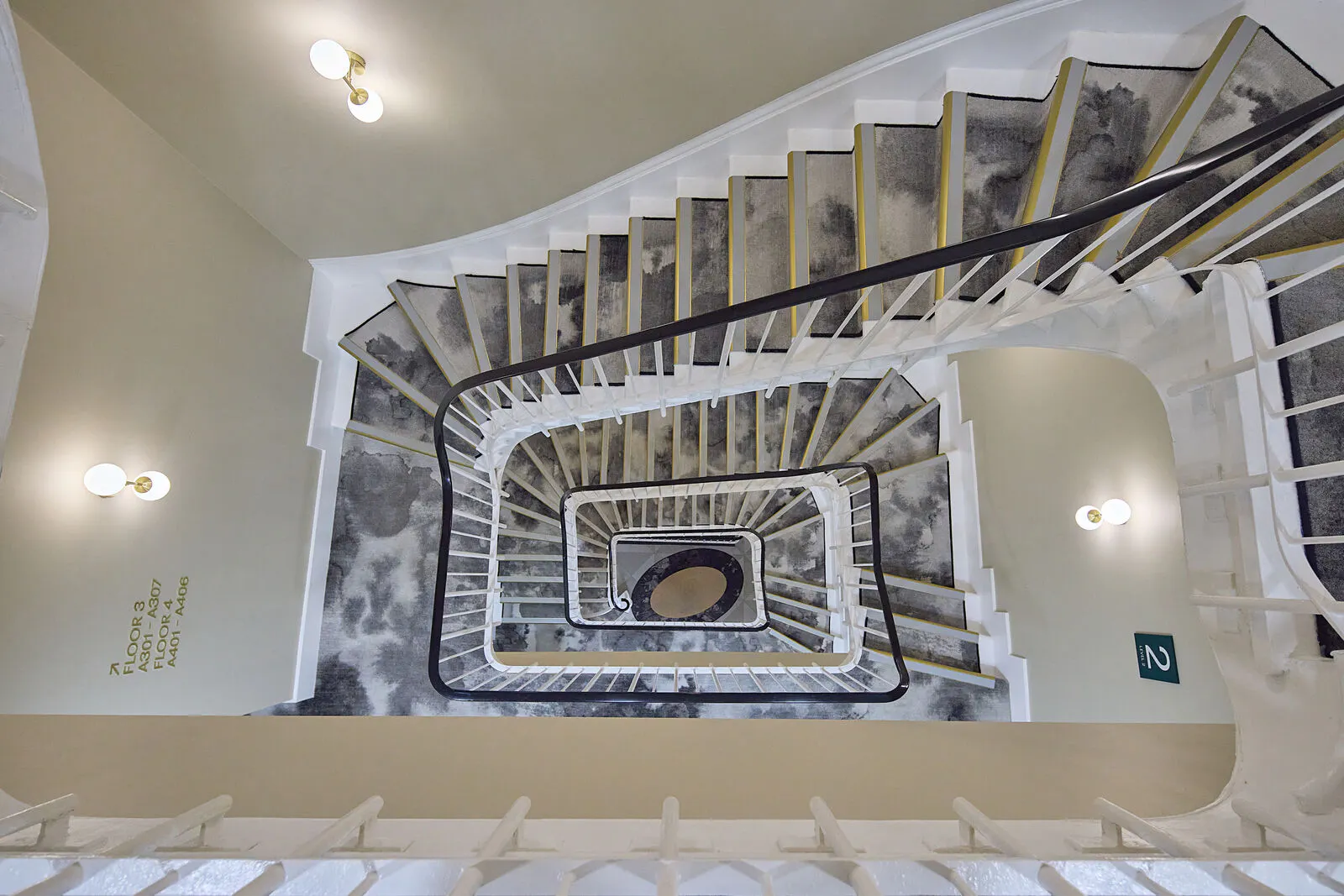 Top down view of The Drey staircase with patterned grey carpet and white railings spiraling through the hotel. Visible text reads "FLOOR 3 A201 A307 FLOOR 4 A401 A406".
